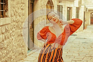 Beautiful stylish girl with long earrings, wearing an orange suit looks at the camera. Traveling around Europe Fashionable woman