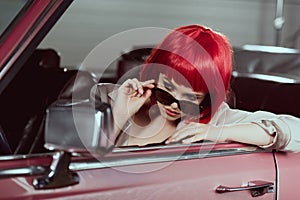 beautiful stylish girl in red wig adjusting sunglasses and looking