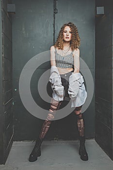 Beautiful stylish grunge woman in white shirt with torn tights and cutly hair standing in the studio