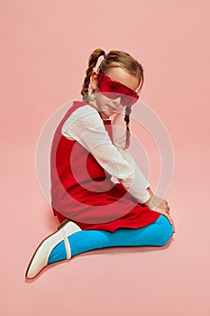 Beautiful, stylish, little girl, child in red dress, blue tights and red glasses posing over pink studio background