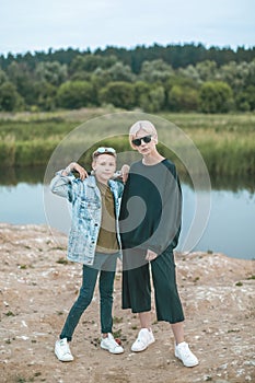 beautiful stylish mother and son standing with baseball bat and looking at camera near lake