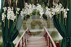 Beautiful stylish wedding aisle pathway with white floral garland hanging from arc with green fashionable curtain near wooden