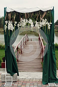 Beautiful stylish wedding aisle pathway with white flowers garland hanging from arc with green fashionable curtain near wooden