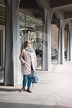 Beautiful stylish woman with bag, sunglasses and mobile phone standing near building on the street of Belgrade, Serbia