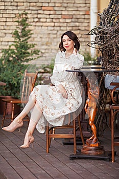 Beautiful stylish woman in beige dress drinking coffee outdoors at the cafe. Portrait of happy female in open air cafe looking at