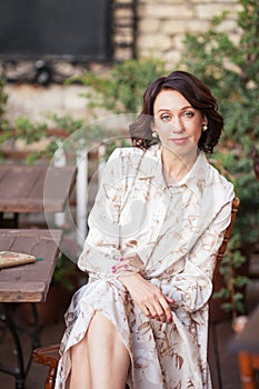 Beautiful stylish woman in beige dress drinking coffee outdoors at the cafe. Portrait of happy female in open air cafe not