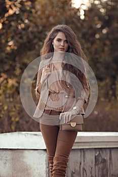 Beautiful stylish woman. Fashion outfit, autumn trend. Young casual brunette walking by cars in street. Fashion girl holding