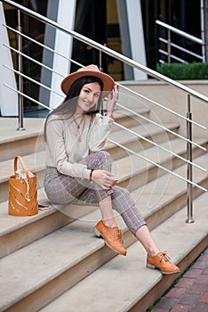 Beautiful stylish woman in fashionable clothes sitting on stairs in cityspace.