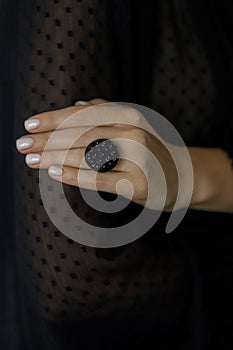 Beautiful stylish woman with modern round black ring on hand and white manicure, close up. Beauty