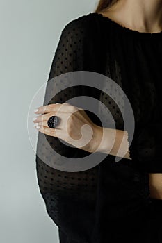 Beautiful stylish woman with modern round black ring on hand and white manicure, close up. Beauty