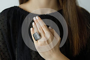 Beautiful stylish woman with modern square black ring on hand and white manicure, close up. Beauty