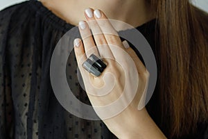 Beautiful stylish woman with modern square black ring on hand and white manicure, close up. Beauty