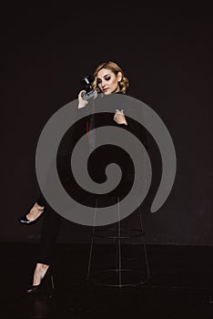 Beautiful stylish woman photographer on a bar stool in a black outfit with a camera in her hands. Soft selective focus