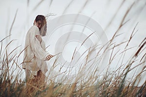 Beautiful stylish woman with windy hair in knitted sweater posing among wild grass. Carefree moment. Fashionable young female