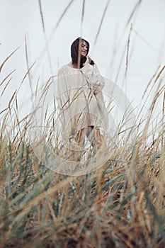 Beautiful stylish woman with windy hair in knitted sweater posing among wild grass. Carefree moment, stylish image. Fashionable