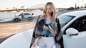 Beautiful and stylish young blonde woman. Portrait with telephone on background of car