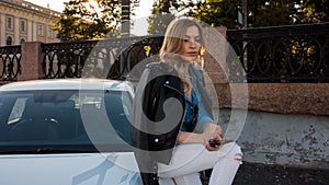 Beautiful and stylish young blonde woman. Portrait with telephone on background of car