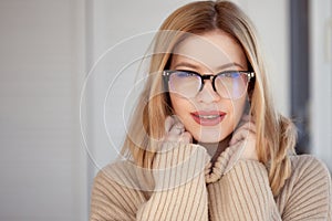 Beautiful and stylish young woman in beige oversize sweater and glasses.