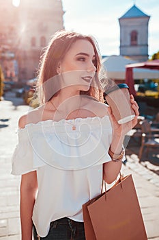 Beautiful stylish young woman with shopping bags chilling on city street and drinking coffee. Summer fashion