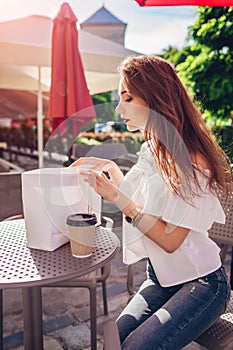 Beautiful stylish young woman with shopping bags chilling in outdoor cafe on city street and checking her purchases.