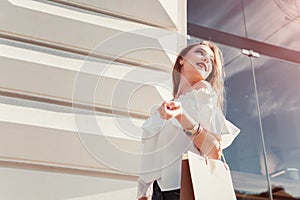 Beautiful stylish young woman with shopping bags walking on city street in summer. Happy girl holding purchases