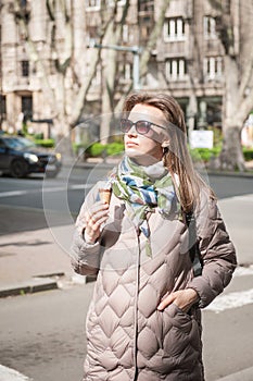 Beautiful stylish young woman with sunglasses eats ice cream walking on the street