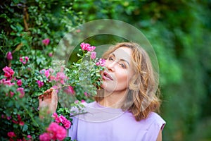 Beautiful successful middle aged woman smelling bloom roses and enjoying in garden outdoors.