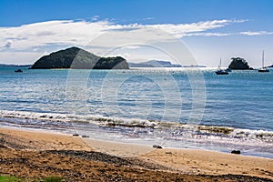 Beautiful summer day on the beach. Leisure boats anchored not far from the shore. Sunlight sparkles on calm water