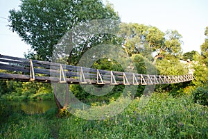 Beautiful summer day shot of an old narrow wooden hanging bridge over Nerl river with high green grass, vibrant vegetation, tall