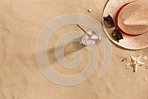 Beautiful summer holiday beach background with straw hat, sunglasses, glass of water and shells on sand background, top view with