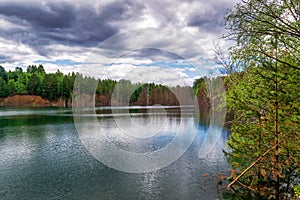 Beautiful summer landscape, forest trees are reflected in calm river water against a background of blue sky and white clouds