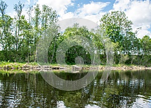 Summer landscape with lake and white cloud reflections in the water, tree silhouettes reflect in the lake water