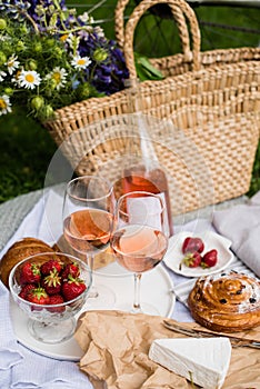 Beautiful summer picnic with strawberries, cheese and rose wine on the lawn in the city park