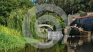 Beautiful summer scene on Este river in Portugal with Roman stone bridge, waterfall and overhanging willow tree.