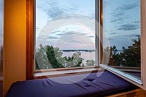 Beautiful summer sundown view from open window. Top of green trees on lake and cloudy sky background