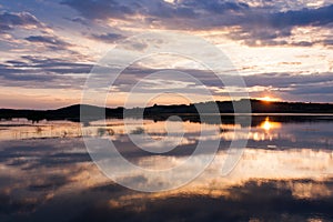 Beautiful summer sunset with cloudy sky and setting sun on the river.