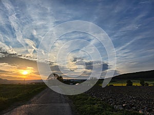 Beautiful summer sunset with a village and a field in the background. Fluffy clouds with a yellow sun.