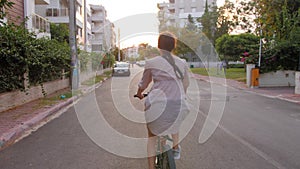 Beautiful summertime mood shot of young woman riding bicycle in stylish outift, pedalling in sunset light