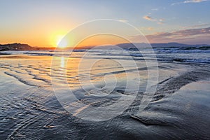 Beautiful summertime view seascape. The wet sand on the sea coast. Unbelievable sunrise. Morning landscape. High waves with foam.