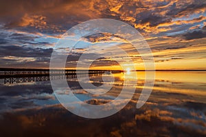 Beautiful sun setting over a wooden pier with puffy clouds blanketing the sky above.