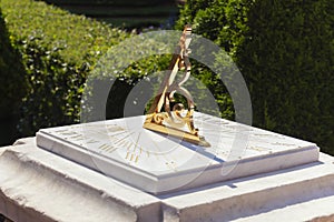 Beautiful sundial on white marble base with gold dial. Golden twisted pointer or gnomon, Close-up