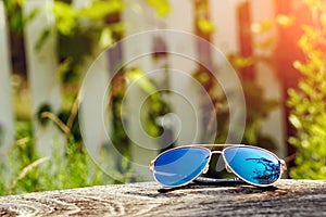 Beautiful sunglasses in gold frame close-up. Lie on a wooden table in the background of a blurred greens. The concept of vacation