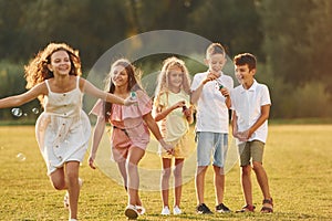 Beautiful sunlight. Group of happy kids is outdoors on the sportive field at daytime