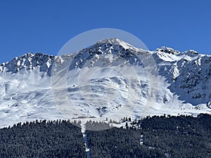 Beautiful sunlight and snow-capped alpine peaks above the Swiss tourist sports-recreational winter resorts