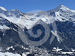 Beautiful sunlight and snow-capped alpine peaks above the Swiss tourist sports-recreational winter resorts