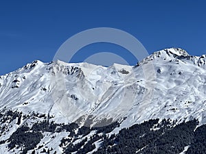 Beautiful sunlight and snow-capped alpine peaks above the Swiss tourist sports-recreational winter resorts