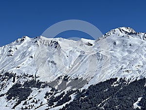 Beautiful sunlight and snow-capped alpine peaks above the Swiss tourist sports-recreational winter resorts