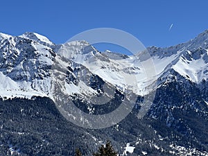 Beautiful sunlight and snow-capped alpine peaks above the Swiss tourist sports-recreational winter resorts