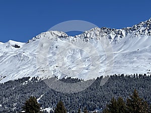 Beautiful sunlight and snow-capped alpine peaks above the Swiss tourist sports-recreational winter resorts