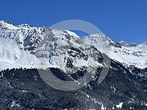 Beautiful sunlight and snow-capped alpine peaks above the Swiss tourist sports-recreational winter resorts